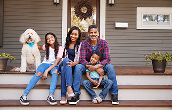 Happy Afro-American family of four with their dog sitting on the porch steps.