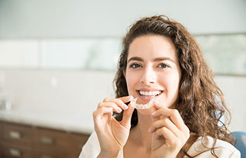 Invisalign adult patient. Happy woman putting on a clear aligner as a part of adult orthodontic treatment at dentistry in Marietta, GA.