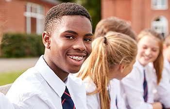 Smiling teenage Afro-american student wearing dental braces chatting with other students