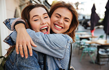 Two happy hugging each other women friends with perfect smiles.