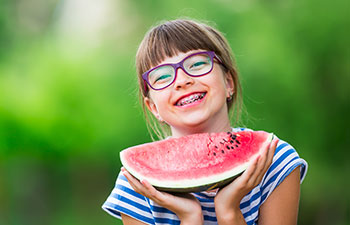 Happy school-girl with dental braces holding a watermelon.