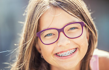 Smiling girl with glasses wearing dental braces.