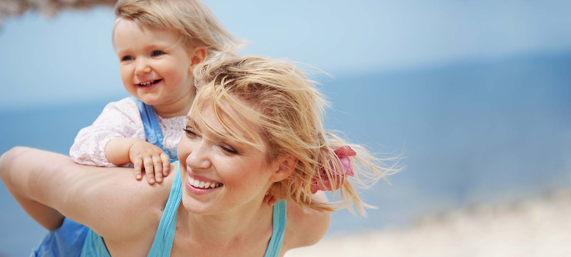 Mother piggybacking her little daughter at the beach.