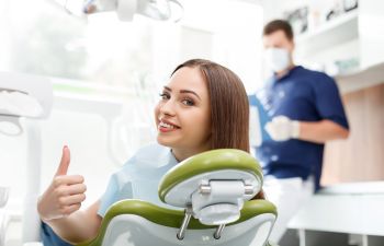 Happy young woman in a dentist chair showing her thumb up.