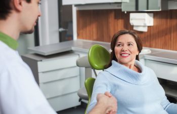 Happy mature woman in a dental chair shaking hands with a dentist.