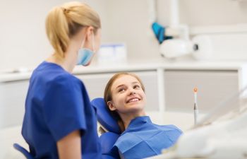 Relaxed teenage girl in a dental chair talking to an orthodontist.