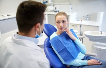 Concerned young woman with dental pain in a dental chair talking to a dentist.
