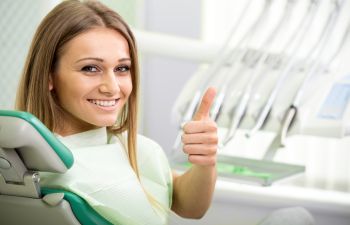 Happy young woman in a dentist chair showing her thumb up.