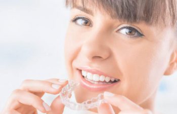 Woman with beautiful smile holding invisalign aligner.