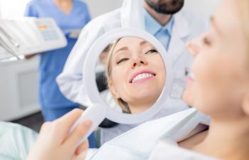 Orthodontic female patient looking at her smile in a mirror after a treatment.